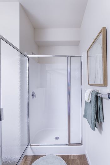 A white bathroom with a glass shower door and a towel hanging on the wall.